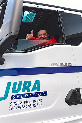 Fahrer im Führerhaus eines LKWs der JURA-Spedition Foto eines Fahrers im Führerhaus eines JURA-Transporters, der den Daumen nach oben zeigt